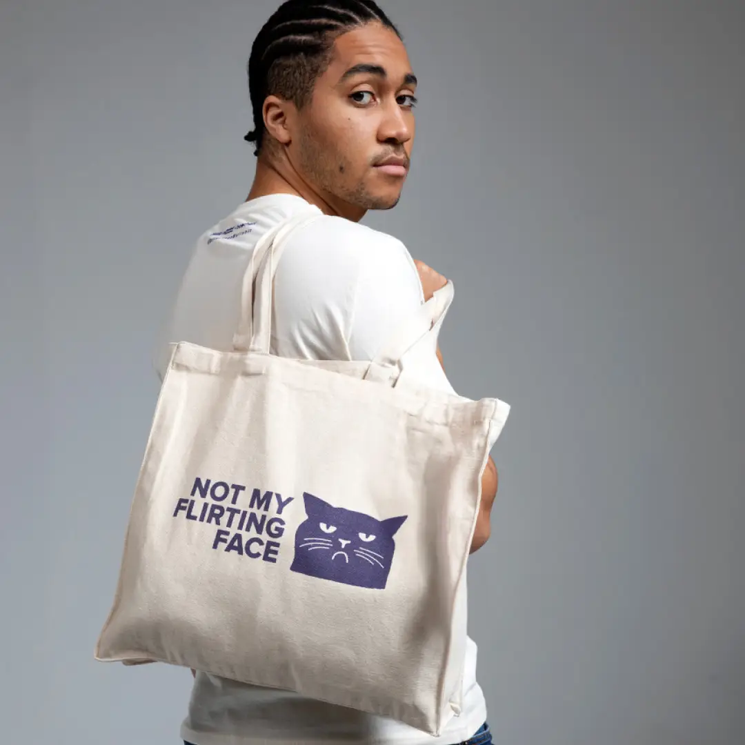Person mit weißem Jutebeutel über der Schulter, darauf ein blaues Katzenmotiv mit dem Text ‚Not my flirting face‘.