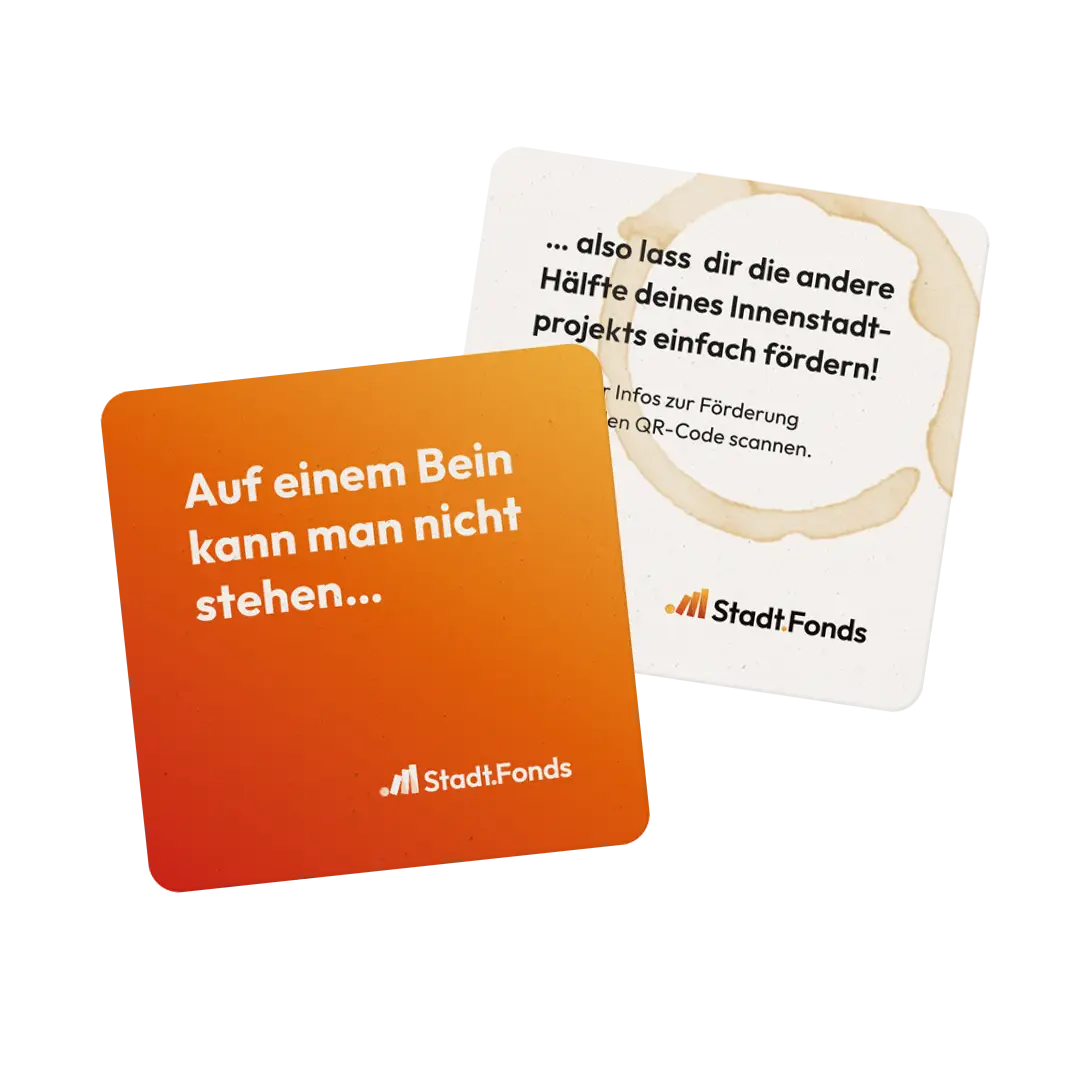 Zwei quadratische Bieruntersetzer, die die Vorder- und R&uuml;ckseite abbilden. Die Vorderseite ist in einem orange-gelben Verlauf und pr&auml;gt die Headline: Auf einem Bein kann man nicht stehen... Erg&auml;nzt wird der Satz durch die R&uuml;ckseite des Bieruntersetzer, welcher hell gehalten ist und sagt: ... also lass dir die andere H&auml;lfte deines Innenstadtprojekts einfach f&ouml;rdern!